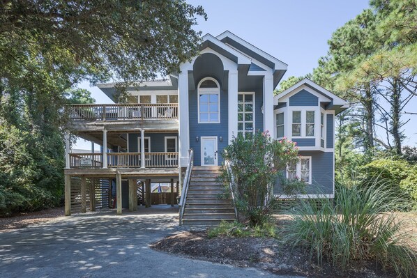 A two-story house with a balcony, a front porch, and a driveway. - 1062 - Beach House Blessings Spacious 5BR Corolla retreat with private pool, deck, and elevator. (Corolla)