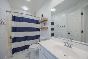 A bathroom with a white toilet, a white sink with a large mirror, and a blue and white striped shower curtain. - 1062 - Beach House Blessings Spacious 5BR Corolla retreat with private pool, deck, and elevator. (Corolla)