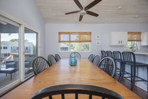 A dining area with a wooden table, chairs, a ceiling fan, and large windows with blinds. - 1062 - Beach House Blessings Spacious 5BR Corolla retreat with private pool, deck, and elevator. (Corolla)