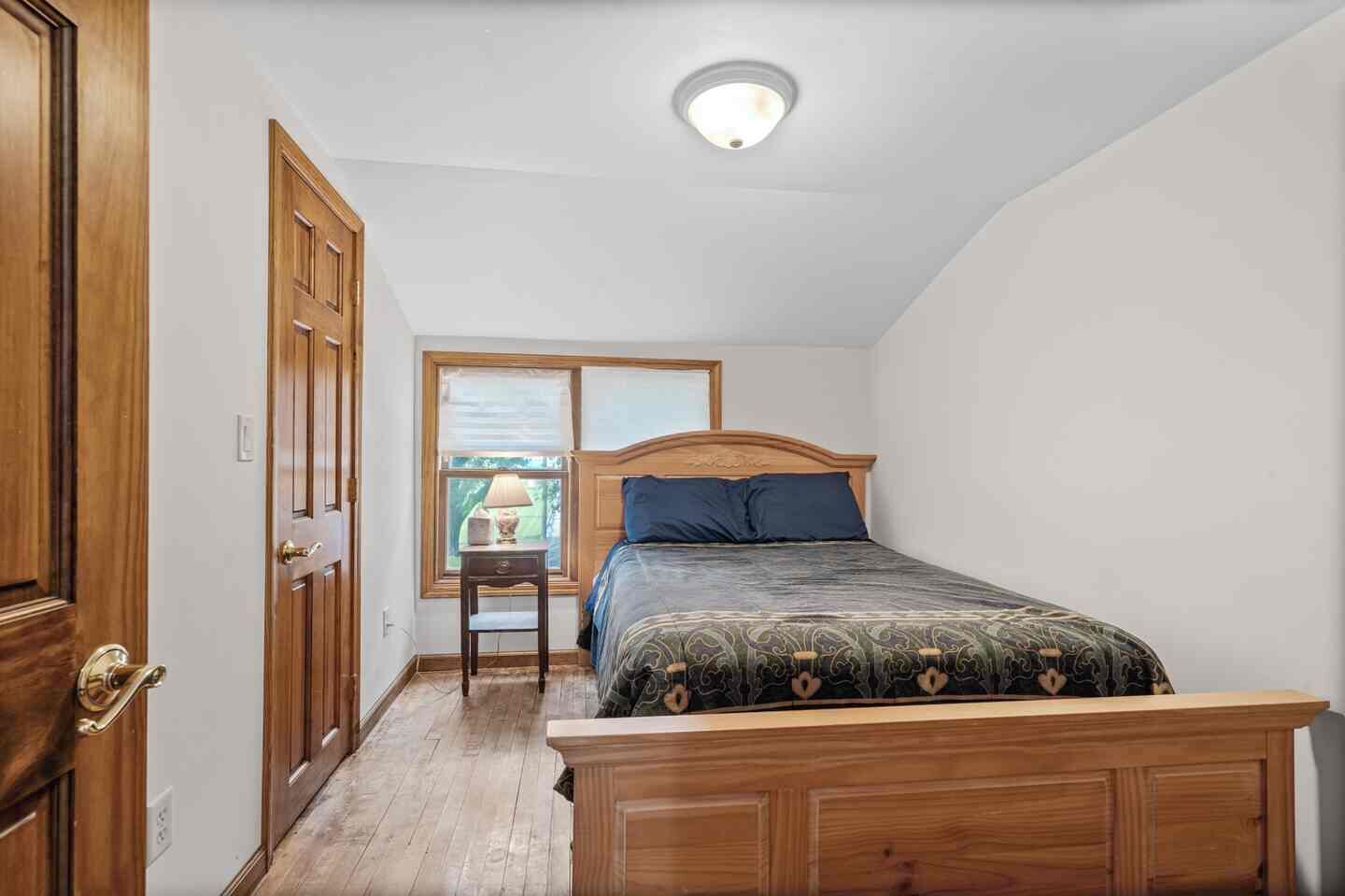 Une chambre à coucher avec un lit en bois, une table de chevet, une fenêtre donnant sur un beau paysage et une porte.