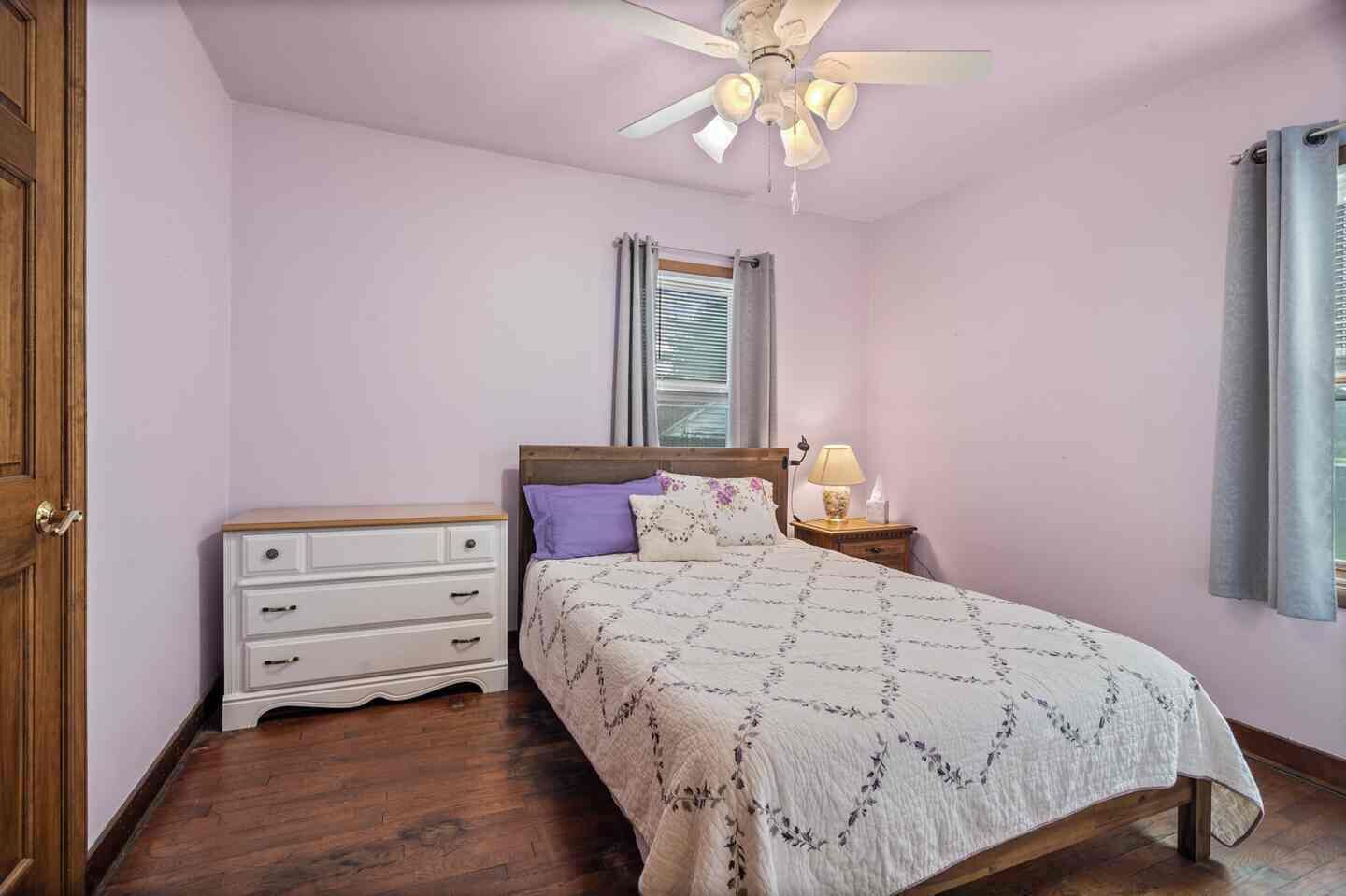 A bedroom with a bed, a nightstand, a dresser, a ceiling fan, and a window with blinds.