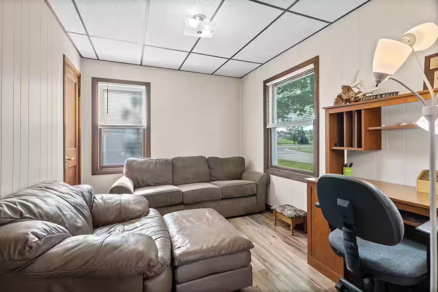 A compact living space with a sofa, a chair, a small table, and a desk with a lamp.