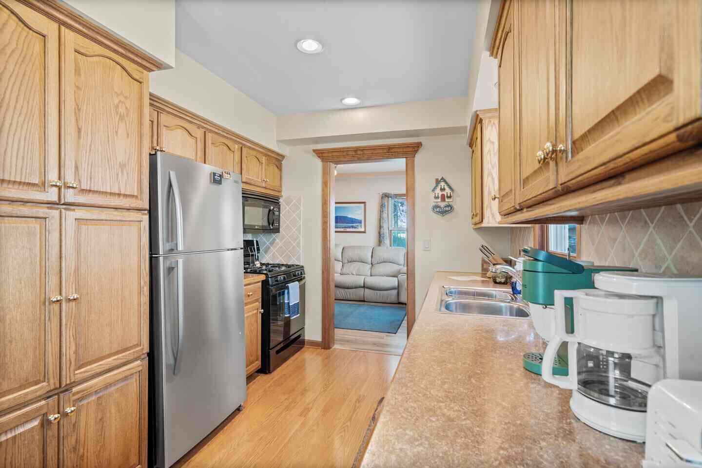 A compact kitchen with wooden cabinets, a stainless steel refrigerator, a stove, and a coffee maker.