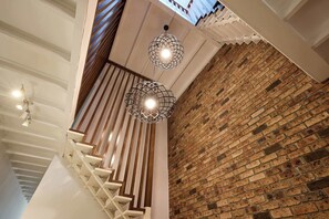 Eine Treppe mit Holzwandhandlauf und weißen Stufen, die zu einem Raum mit Backsteinwand und geneigter Decke führt.