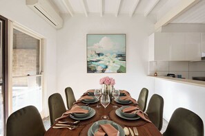 A dining room with a table set for six, a painting above the table, and a kitchen area to the right. - 3BR Glebe House | Garage Parking, Near Fish Market (Glebe)