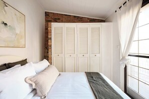 A bedroom with a bed, a brick wall, white doors, and a window with curtains. - 3BR Glebe House | Garage Parking, Near Fish Market (Glebe)