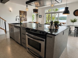 A modern kitchen with a central island, stainless steel appliances, pendant lighting, and a view of the outdoors.