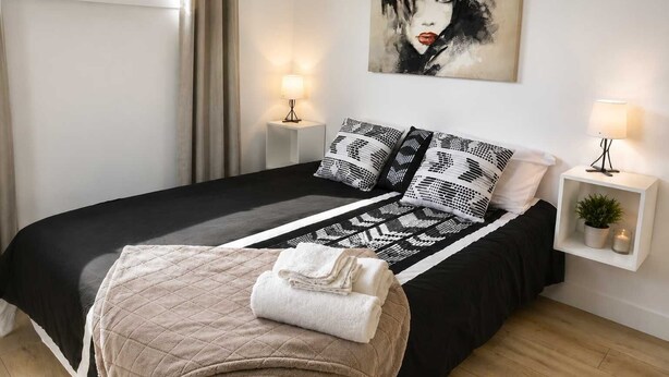 Un dormitorio moderno con una colcha estampada en blanco y negro, un plaid acolchado y un cuadro sobre la cama.