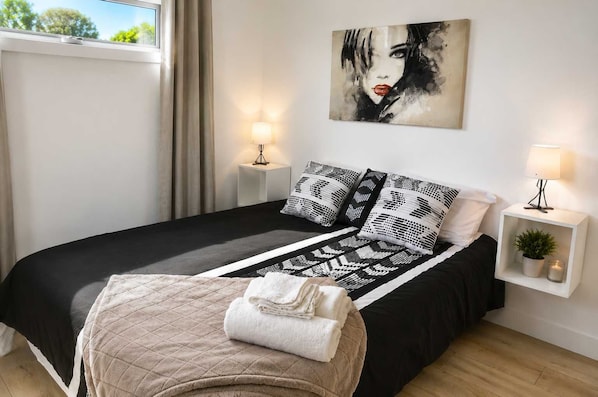 A modern bedroom with a black and white patterned bedspread, a quilted throw, and a painting above the bed.