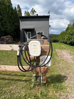 An electric vehicle charging station with a white box labeled 'Atti Home' in front of a house.