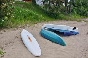 A sandy beach with two kayaks and a surfboard.