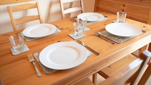 A wooden dining table set with white plates, cutlery, and clear glasses on coasters.