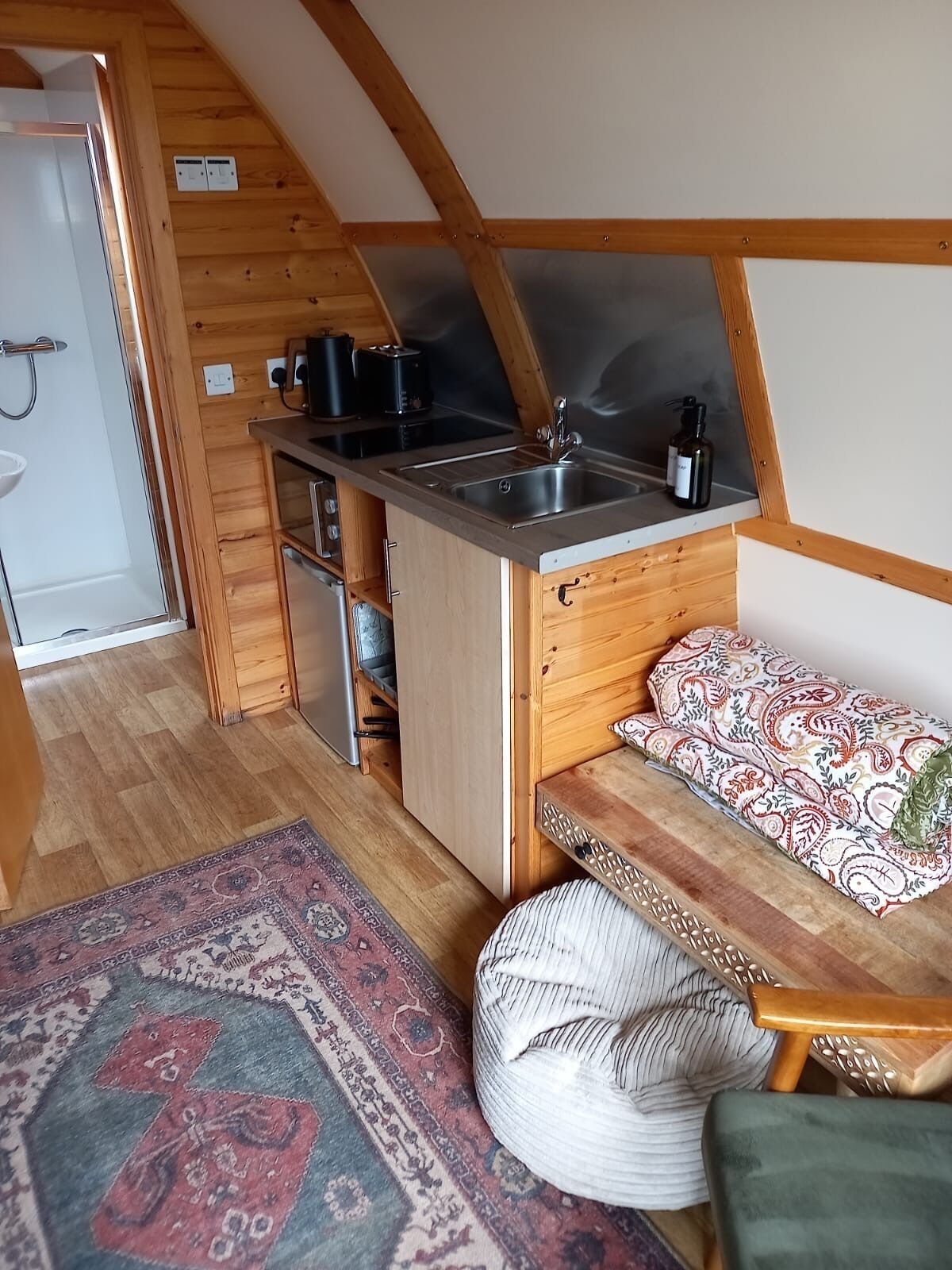 A compact kitchen with a sink, wooden cabinets, and a small dining area with a bench and cushions.