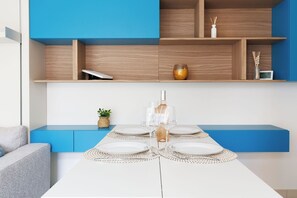 Ein moderner Essbereich mit einem weißen Tisch für vier Personen, einer blauen Bank und Holzregalen darüber.