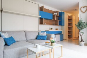 Ein modernes Wohnzimmer mit einem grauen Sofa, einem weißen Couchtisch und einer Küchenzeile mit blauen Schränken.
