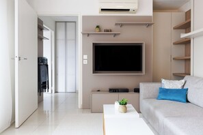 A modern living room with a flat-screen TV, a grey sofa with a blue pillow, a coffee table with a plant, and a white door leading to a hallway. - Upstays Le Suquet 1Br with Ac and Terrace (Cannes)