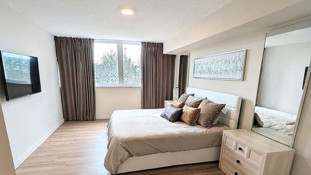 Une chambre à coucher avec un lit, une commode, un téléviseur et une fenêtre avec des rideaux.