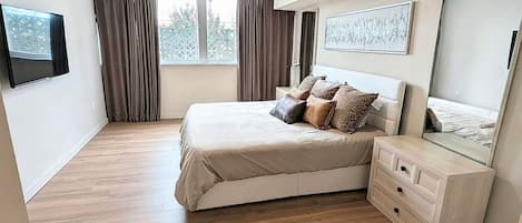 Quarto com cama, cômoda, televisão e janela com cortinas.