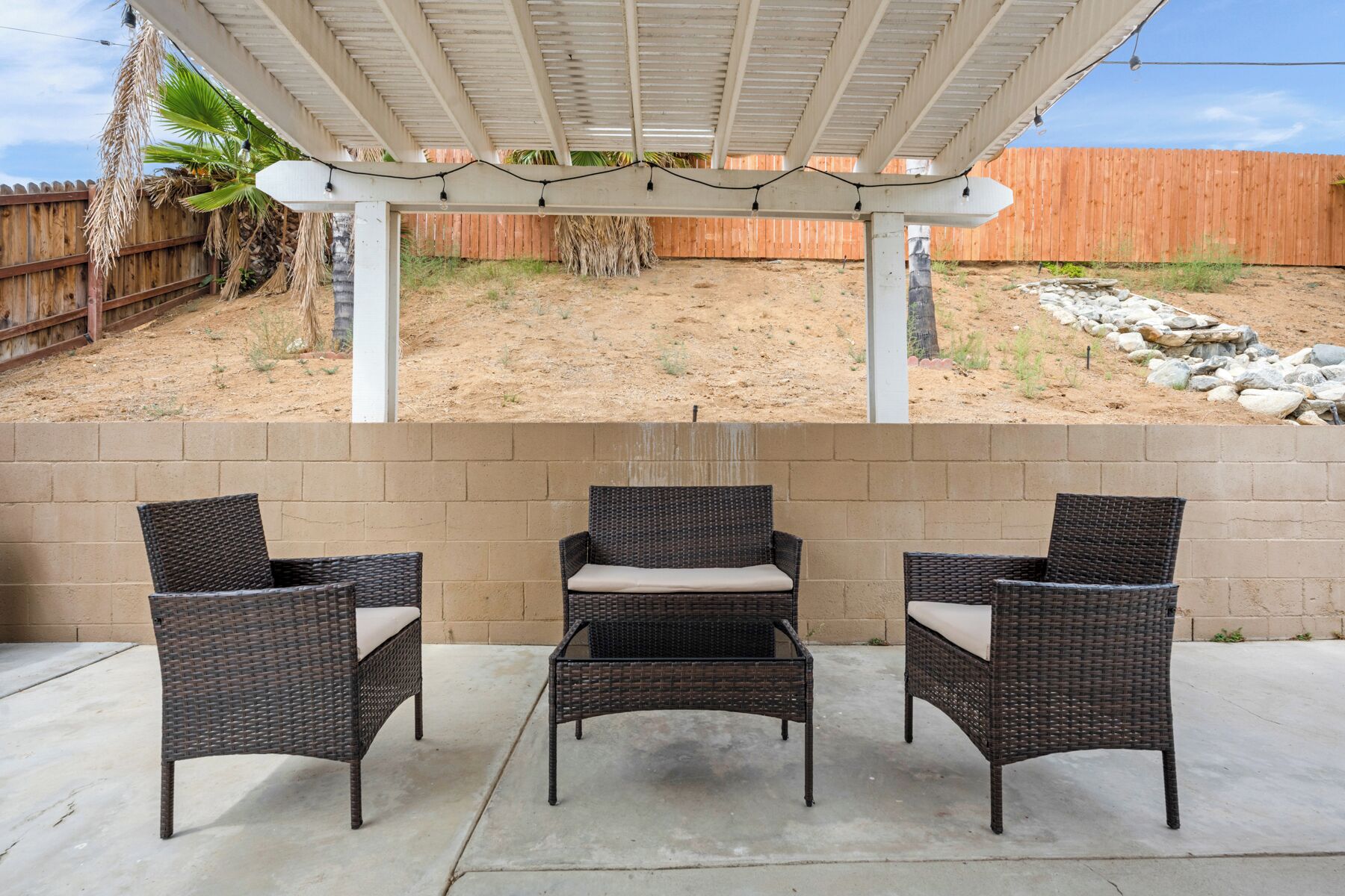 Un espace extérieur aménagé en terrasse, avec trois chaises en osier et une pergola au-dessus.