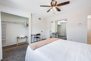 A hotel room with a bed, a desk, a chair, a wardrobe, and a ceiling fan.