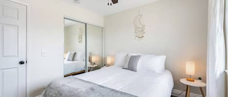 A hotel room with a bed, a ceiling fan, a mirror, bedside lamps, and a door.