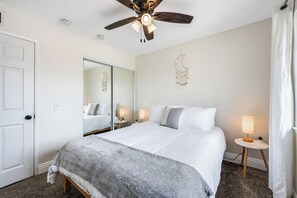 A hotel room with a bed, a ceiling fan, a mirror, bedside lamps, and a door. - Newell's Nest, Large Pool, Games BBQ Island, 3 bedroom, Outdoor Seating, Parking (Riverside)