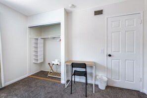 A room with a white door, a small table with a chair, a white trash bin, and a closet with a hanging organizer. - Newell's Nest, Large Pool, Games BBQ Island, 3 bedroom, Outdoor Seating, Parking (Riverside)