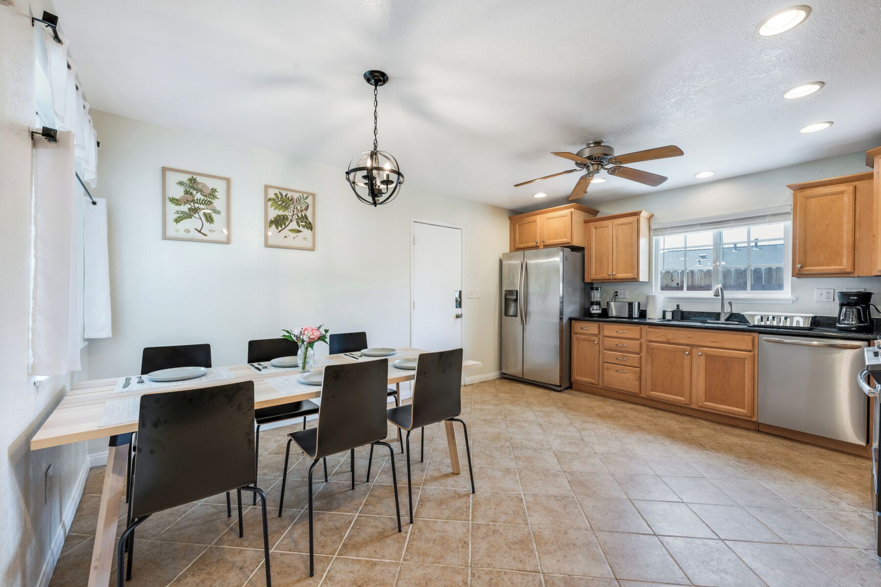 A modern kitchen with a dining area, featuring a stainless steel refrigerator, wooden cabinets, and a ceiling fan.