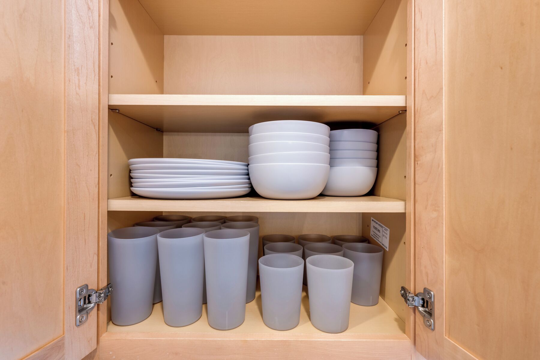 Un meuble en bois doté d’étagères où sont rangées des assiettes blanches, des bols et des tasses grises.