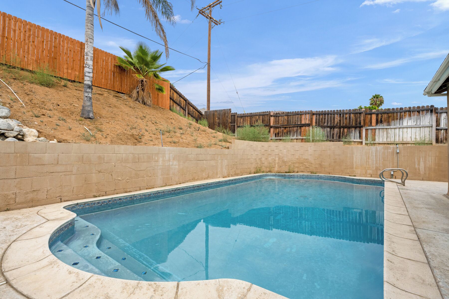 A swimming pool with a curved edge, surrounded by a brick wall and a wooden fence.
