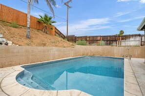 A swimming pool with a curved edge, surrounded by a brick wall and a wooden fence.