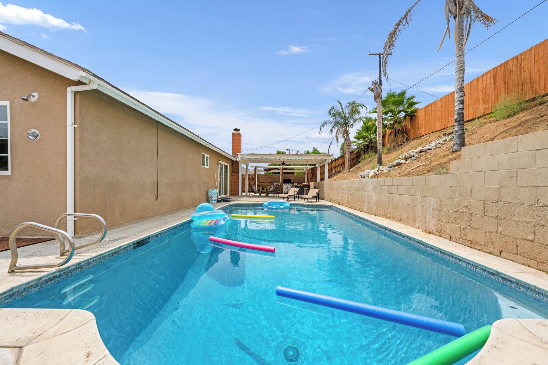 Une piscine à l’eau d’un bleu limpide, entour ée d’un mur de couleur beige et d’une clôture en bois.