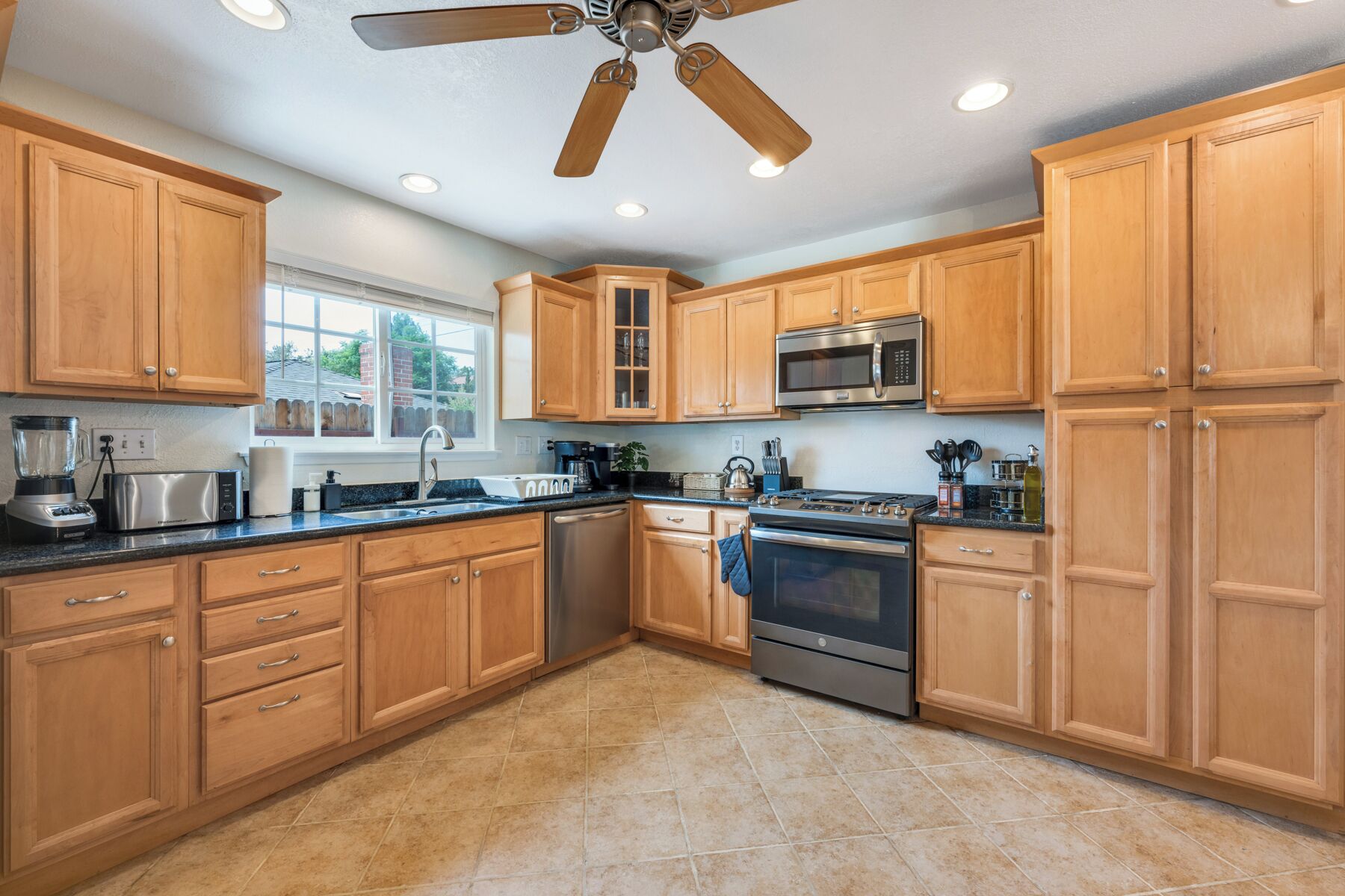 A kitchen with wooden cabinets, a stainless steel microwave, a stove, and a ceiling fan.
