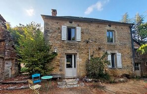 A stone building with a door and windows, a bench, and a small table. - Charmante maison au calme (Jayac)