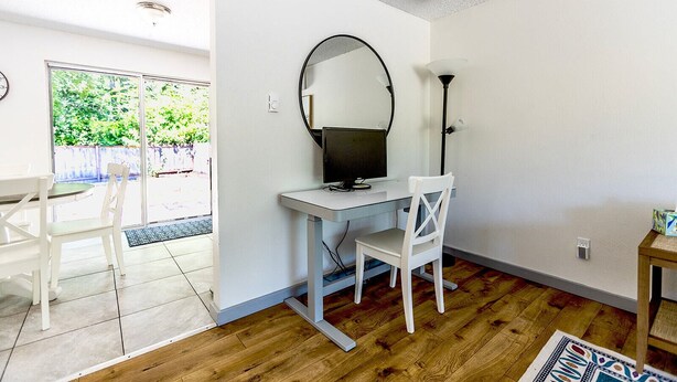 A small, bright room with a desk and chair, a large mirror, and a lamp. There is a window with a view of greenery outside. - Cozy 2 bed - Close to Town  Pet Friendly (Gig Harbor)