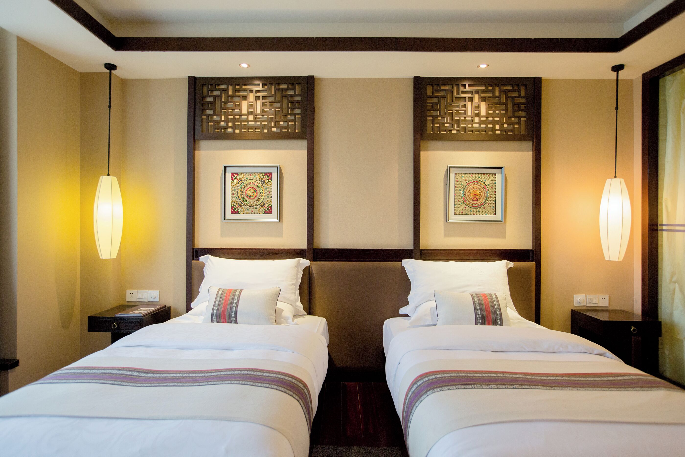 Quarto de hotel com duas camas, um painel decorativo na parede e duas obras de arte emolduradas.