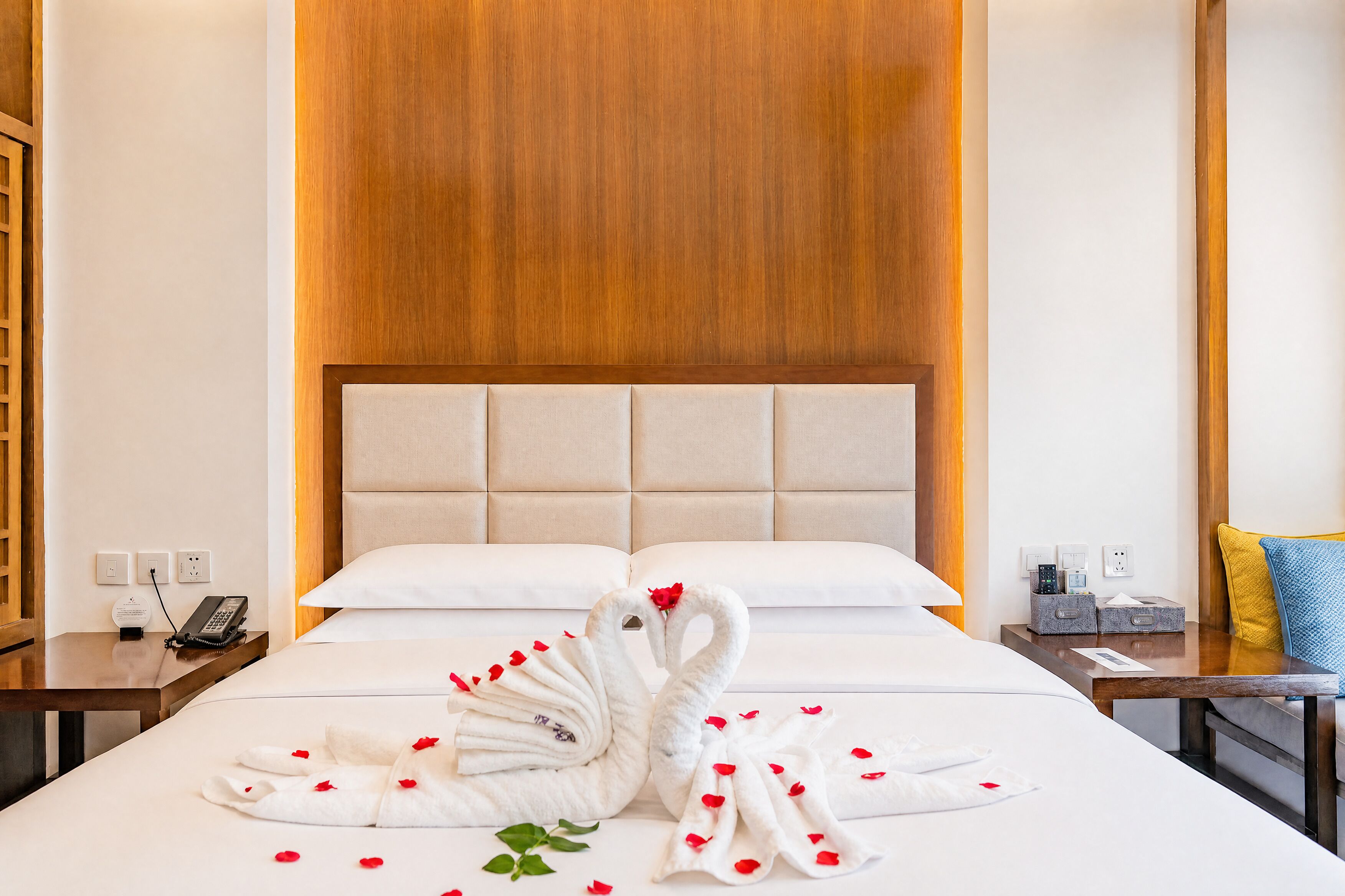 Habitación de hotel con cama, cabecera de madera, mesita de noche con teléfono y en la pared un enchufe.