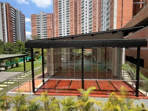 A modern building with a covered outdoor area, glass walls, and a red-tiled floor. - In Sabaneta | Apartment | Security | Extra Services | Parking | Overlooking a Nature Reserve (Sabaneta)
