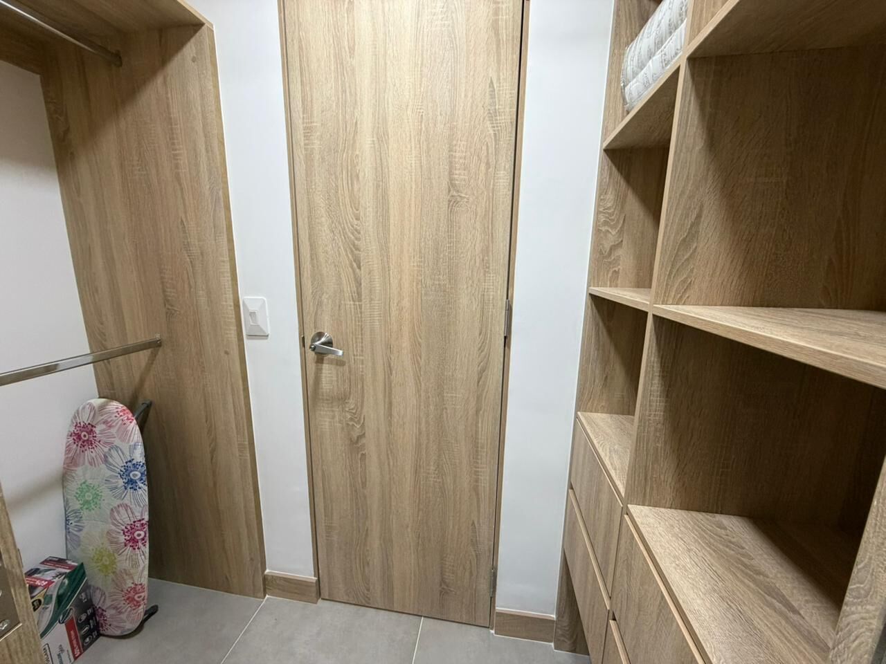 A wooden wardrobe with a door, a shelf unit, and a patterned ironing board.