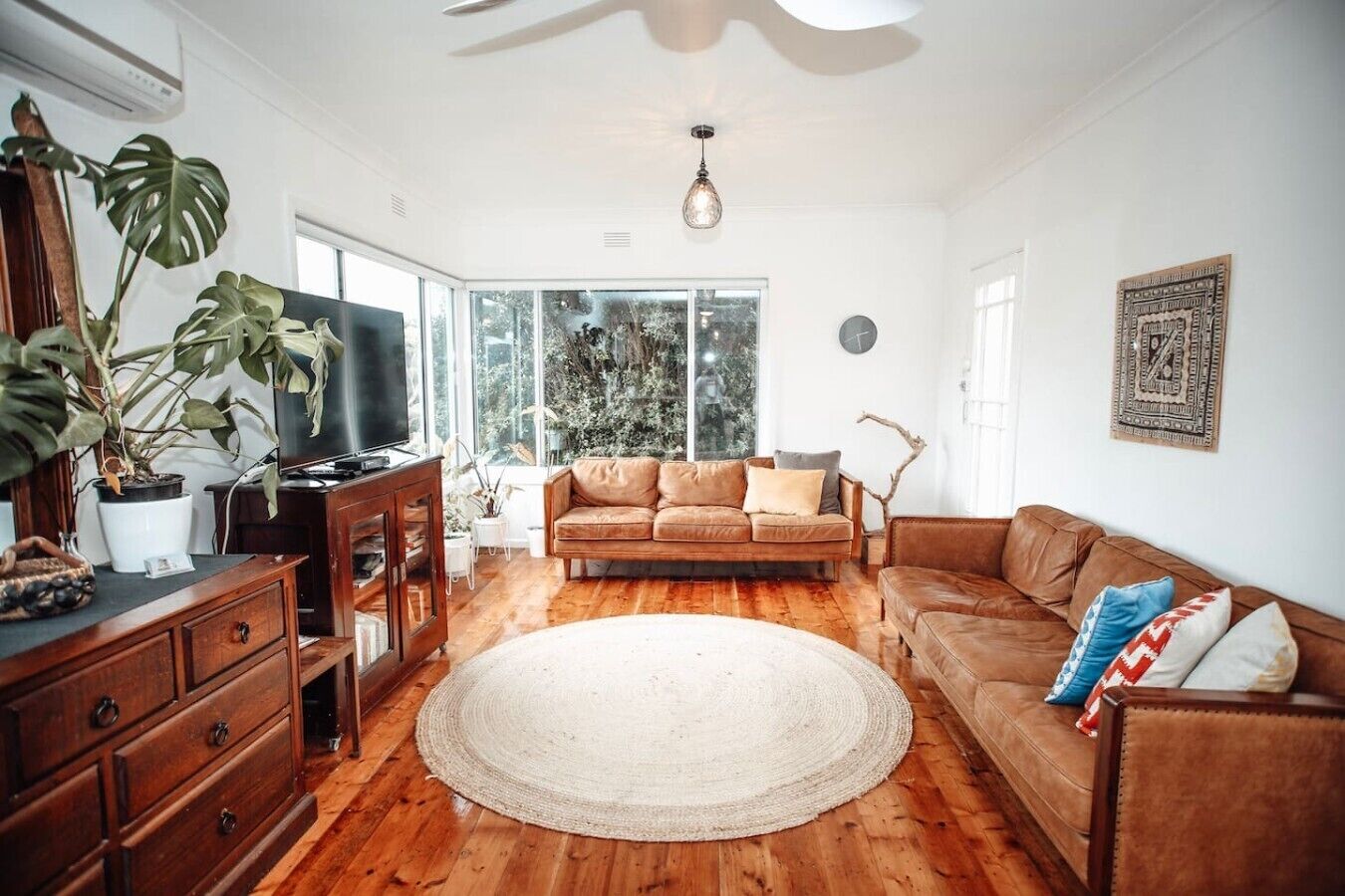 Un salon avec un canapé en cuir marron, un tapis rond, un meuble en bois et un téléviseur.