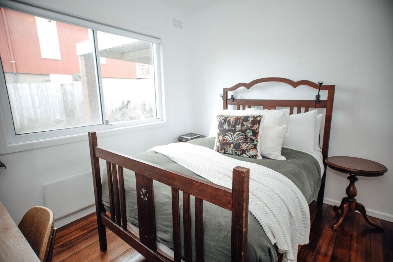 A bedroom with a wooden bed, a bedside table, a chair, and a window.