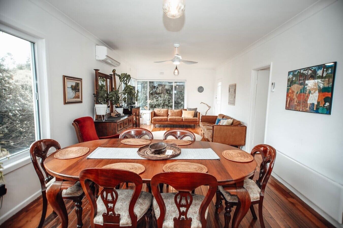 A dining area with a wooden table and chairs, a ceiling fan, and a view of the outdoors.