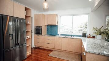 A modern kitchen with wooden cabinets, a stainless steel refrigerator, a built-in oven, and a large window providing a view.