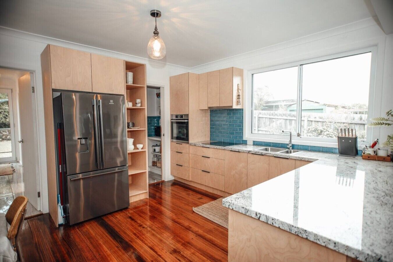 A modern kitchen with a large island, stainless steel appliances, and a view through the window.