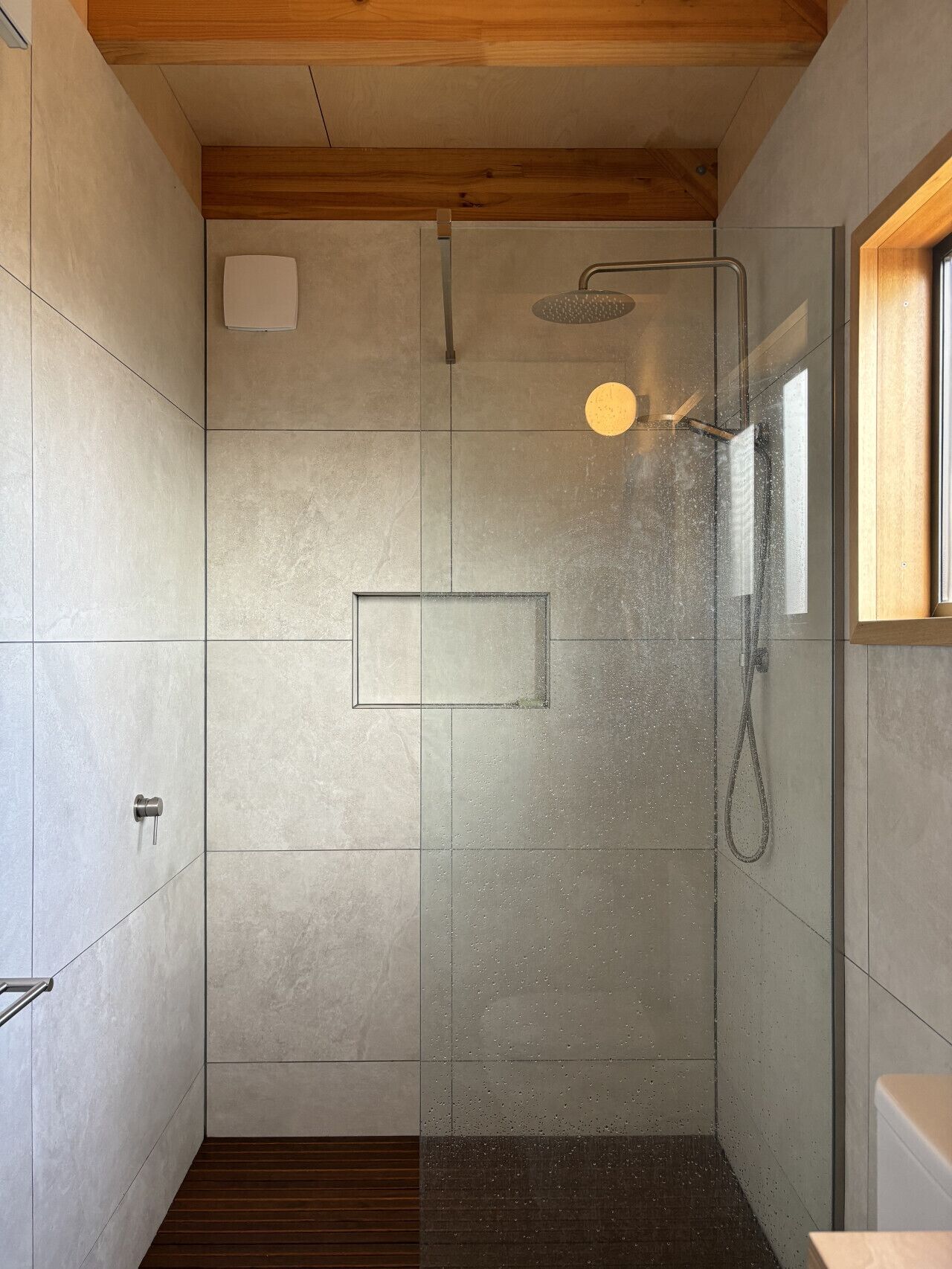 Une douche moderne dotée d’une porte en verre, d’un pommeau de douche à main et d’un panneau de commande fixé au mur.
