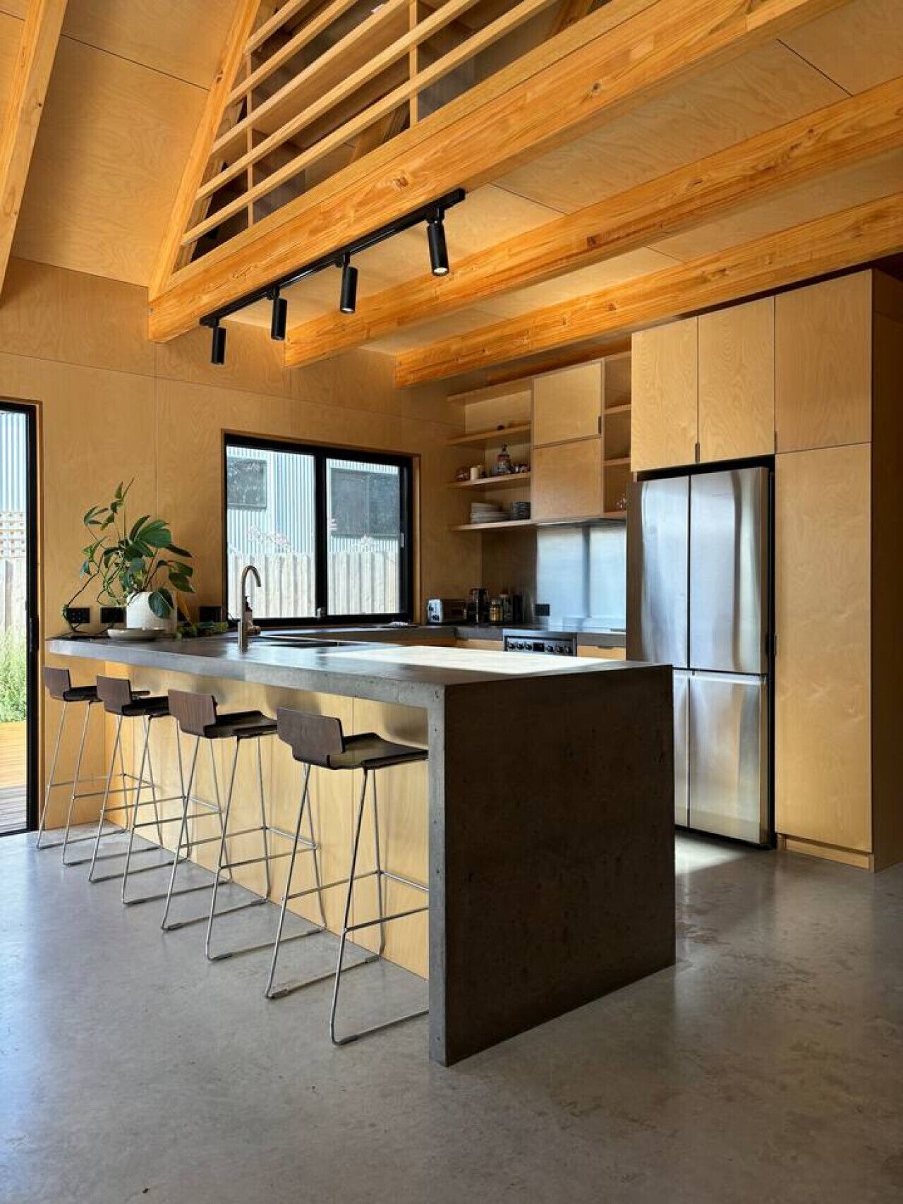 Una cocina moderna con una isla central, taburetes de bar, electrodomésticos de acero inoxidable y techo de madera.
