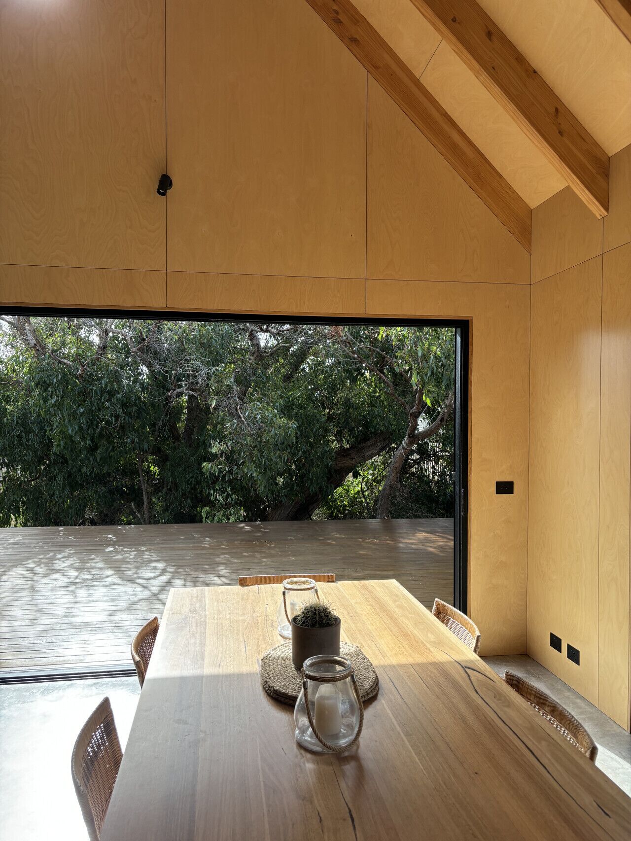 Un intérieur moderne avec une table en bois, des chaises et une vue sur un paysage naturel, visible à travers une grande fenêtre.