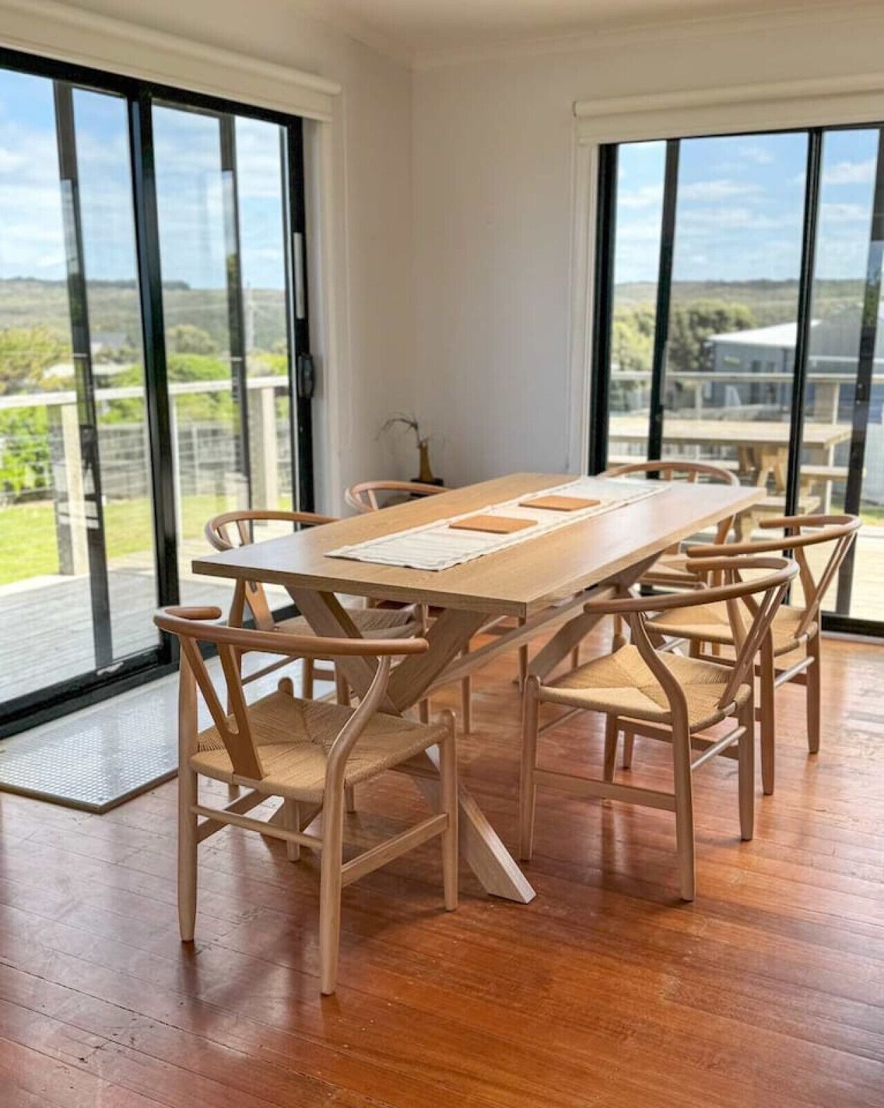 A dining area with a wooden table and chairs, large windows, and a view of the outdoors.