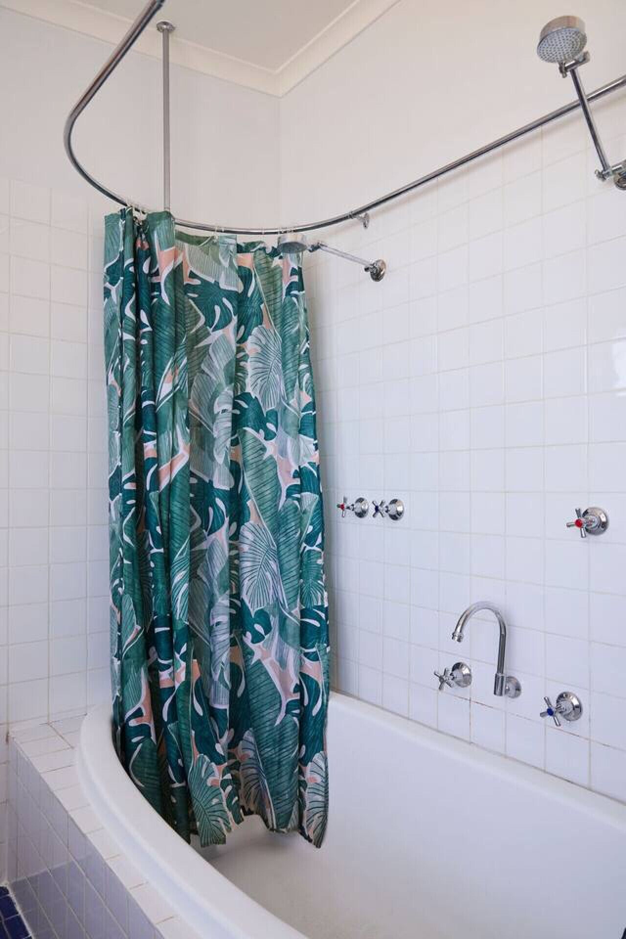 A shower with a curved showerhead and a curtain with a leaf pattern.