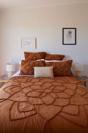 Una cama con colcha y almohadas marrones a juego, una almohada blanca decorativa y dos lámparas de noche a cada lado.
